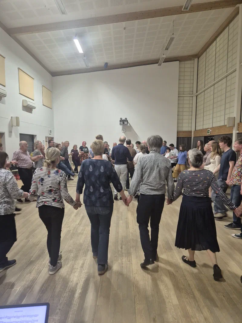 Dancers holding hands in a line across a hall