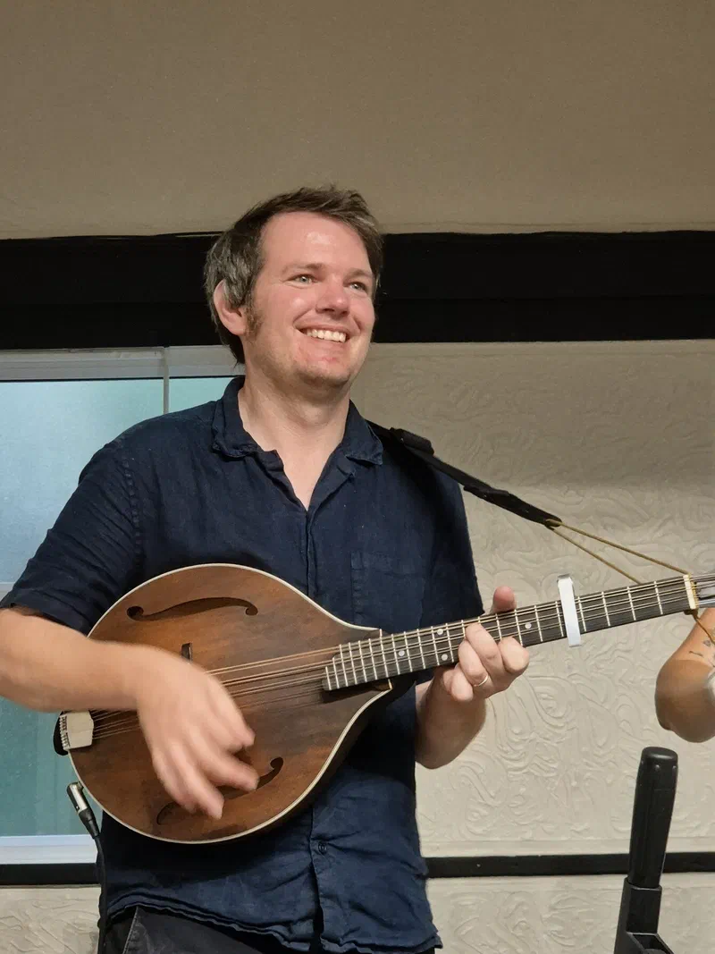 Tom smiling and playing the mandolin