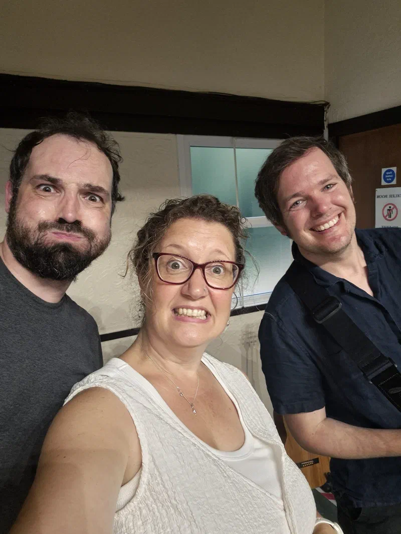 Dom, Sarah and Tom grinning at the camera in a village hall