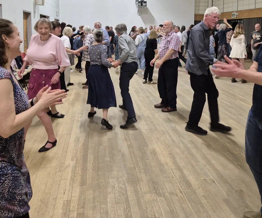 A full circle of dancers clapping along in a village hall